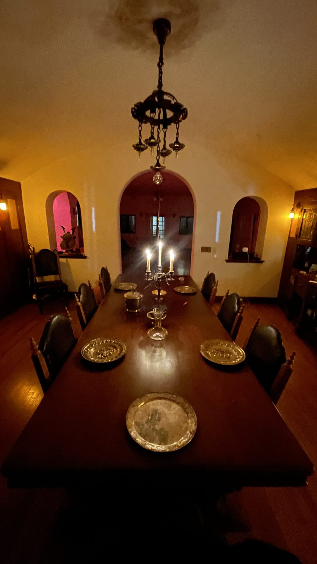 A long candlelit dining table set with brass chargers beneath an arched, vaulted ceiling, a table set and waiting.